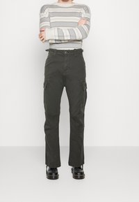 Cargo broeken van donkergroen katoenen stof, met rechte pijpen, zijzakken en een knoopsluiting. Gecombineerd met een gestreepte grijze trui.