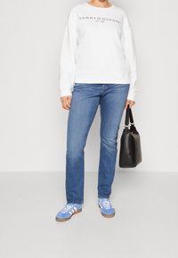 Sudadera blanca con el logo de "Tommy Hilfiger", combinada con jeans azules y zapatillas de deporte de color azul claro. Lleva un bolso negro.