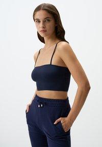 Navyblauwe cropped top met dunne spaghettibandjes, een gladde textuur en een aansluitend ontwerp, gecombineerd met navy joggerbroeken met zijzakken.