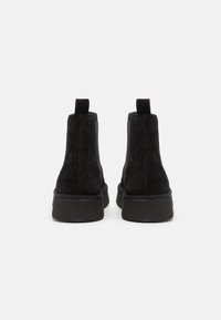 Botas de tobillo de ante negro con un acabado texturizado, suela de goma plana y tiradores en la parte trasera para ponerlas fácilmente. Acentos suaves en los laterales.