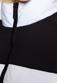 Giacca a blocchi di colore bianco e nero con colletto alto, dotata di una zip nera e texture liscia. Il design è moderno e minimale.