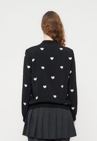 Μαύρο φούτερ με κρεμ μοτίβο καρδιάς παντού. Διαθέτει ριμπ γιακά και μανσέτες. Το μοντέλο φοράει πλισέ γκρι φούστα.