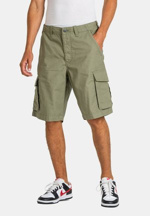 Green cargo shorts made of cotton blend fabric, featuring side pockets, a relaxed fit, and a straight cut, paired with black and white sneakers.