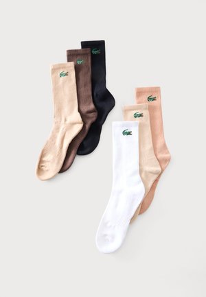 Sei calzini a coste beige, marrone, nero, bianco e pesca, ognuno con un piccolo logo di coccodrillo verde vicino al bordo.