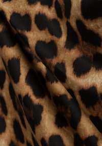 Tessuto con stampa leopardata in tonalità di marrone e nero, dalla texture morbida, caratterizzato da una miscela di macchie nere irregolari su uno sfondo beige.
