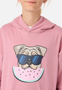 Rosa huvtröja med en grafik av en hund som bär blå solglasögon och håller en skiva vattenmelon med svarta frön. Mjuk tyg, avslappnad design.