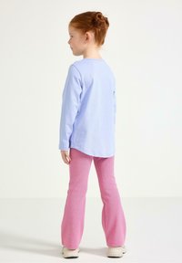 Lyseblå langærmet skjorte med rundet kant sammen med lyserøde, udvidede bukser. Hvide sneakers synlige, tekstureret stof i begge beklædningsgenstande.