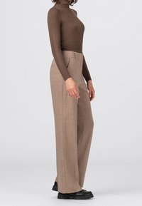 Bruine geribbelde coltrui gecombineerd met lichtbruine wijde broek. De broek heeft een gestructureerde stof en zijzakken. Zwarte schoenen met dikke zool.