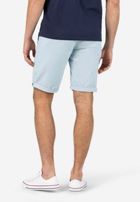 Hellblaue Shorts mit umgeschlagenen Säumen, aus leichtem Stoff. Getragen mit weißen Sneakers mit roten Akzenten. Rückansicht, lässige Passform.