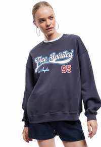 Donkergrijze sweatshirt met blauwe en rode "Free Spirited" graphic, met een ribgebreide kraag en manchetten, gecombineerd met marineblauwe shorts.