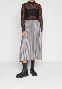 Černý krajkový crop top s dlouhým rukávem přes plisovanou šedou sukni střední délky; doplněný černými kotníkovými botami s robustní podrážkou.