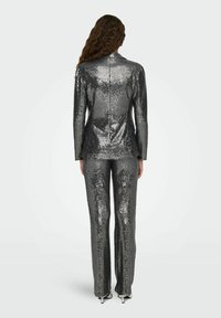 Traje de lentejuelas plateadas que incluye una chaqueta ajustada con cuello de pico y pantalones a medida, ambos con una superficie reflectante y texturizada.