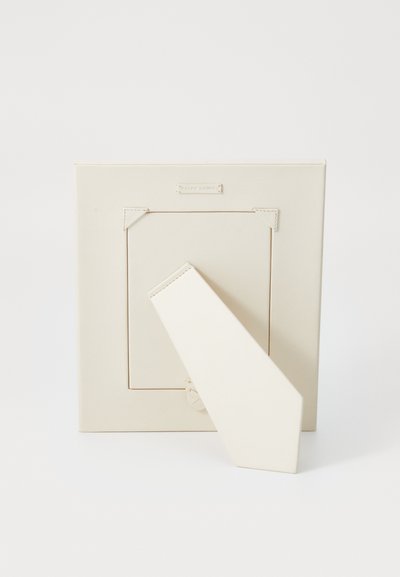 Cornice fotografica beige con una finitura in pelle liscia, dotata di un supporto triangolare e di una piccola etichetta con marchio nella parte superiore.