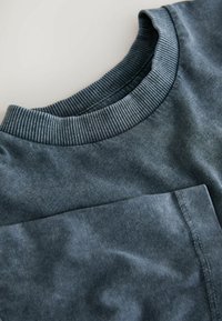 Mørkeblå bomulds t-shirt med ribbet rund hals og en brystlomme med synlige syningsdetaljer. Blødt, tekstureret stof.