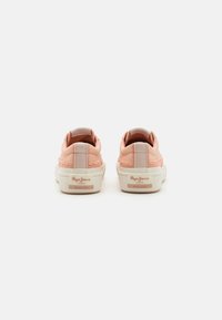 Pink canvas sneakers with white rubber soles. Back view features padded collars and branded tags. Textured detailing along the sides.