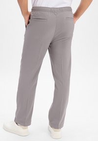 Grijze broek met een elastische tailleband, twee achterzakken, rechte pijpen en een gladde stoftextuur. Draag met witte sneakers.