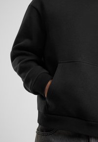 Schwarzer Sweatshirt mit einem runden Halsausschnitt, gerippten Bündchen und einer Vordertasche. Strukturiertem Stoff sichtbar, mit einer lockeren Passform.