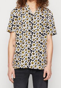 Koszula krótki rękaw, zapinana na guziki, w czarnym kolorze z białymi i żółtymi wzorami kwiatowymi, w tym literami i znakami pokoju, wykonana z lekkiego materiału.