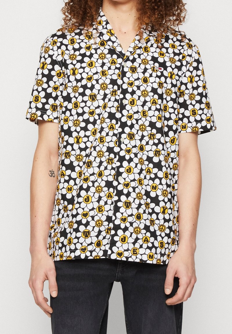 Koszula krótki rękaw, zapinana na guziki, w czarnym kolorze z białymi i żółtymi wzorami kwiatowymi, w tym literami i znakami pokoju, wykonana z lekkiego materiału.