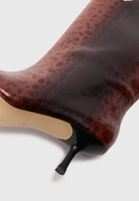 Ruskeat nahkaiset nilkkasaappaat, joissa on teksturoitu käärmeennahkakuosi, terävä kärki ja stiletto-korko. Pohja on neutraali beige.