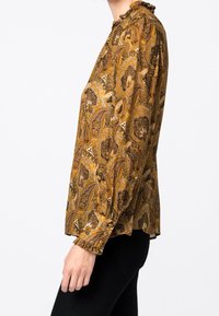 Blouse à manches longues en jaune moutarde avec motif paisley, décolleté froncé et poignets élastiques. Tissu léger et texturé.
