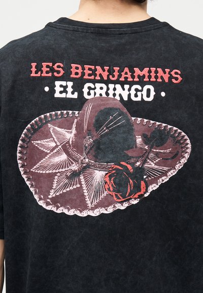 Μαύρο μπλουζάκι με μεγάλο σομπρέρο, κόκκινο τριαντάφυλλο και το κείμενο «Les Benjamins El Gringo» στην πλάτη, φορεμένο από άτομο που κοιτάζει προς τα πίσω.