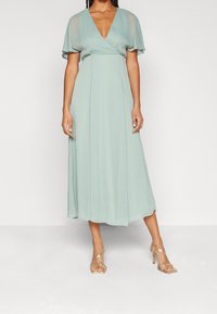 Robe verte clair mi-longue avec un décolleté en V et des manches courtes à patte d'eph. Fabriquée dans un tissu fluide, elle présente une taille cintrée et une jupe évasée.