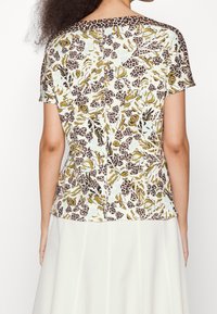 Top de manga corta con un diseño de flores y estampado de leopardo en verde, marrón y azul claro. Tejido suave, corte relajado, cuello redondo y ligera textura.