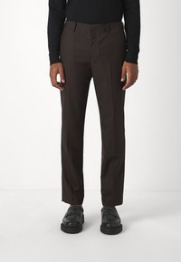 Brune, skreddersydde bukser med et subtilt stripe mønster, flat front, sidelommer og rett ben-design. Kombinert med svarte slip-on sko.