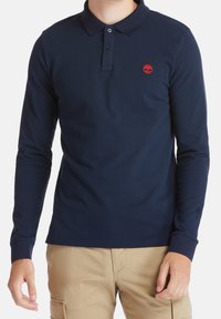 Marinblå långärmad polo tröja i texturerad bomull, med en knäppt krage, en broderad röd logotyp och ribbade ärmslut.