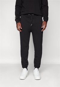 Sorte joggebukser laget av mykt stoff med snor i midjen og elastiske mansjetter. Båret med hvite joggesko, som viser en uformell stil.
