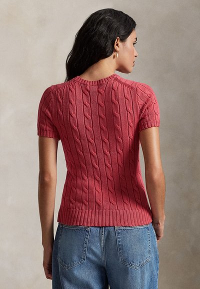 Krótki rękaw, sweter z grubym splotem w kolorze koralowym z prążkowanym obszyciem. Charakteryzuje się dopasowanym krojem i fakturowanym wzorem. Noszony z jeansami z wysokim stanem.