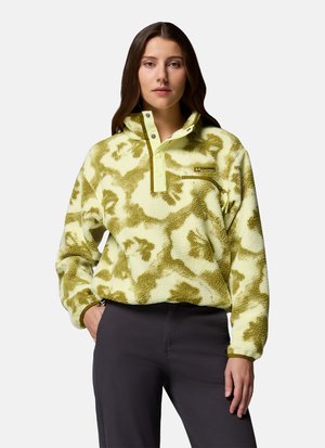 Woman wearing green and cream patterned fleece pullover with front snap buttons and zippered pocket, paired with dark pants.