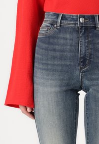 Høyt midje denim jeans i blått med lett falming, med front knapp åpning, belte løkker og sidelommer. Kombinert med en rød topp.
