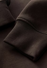 Mørkebrune sweatshirtærmer med ribbede ærmegab og glat stoftekstur i close-up.
