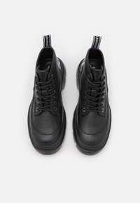 Par de botas de tobillo de cuero negro con cordones, suelas de goma gruesas y lengüetas con el logo en la parte posterior sobre fondo blanco.