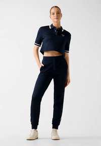 Polo court marine avec col et manches blancs, accompagné d'un pantalon de jogging marine. Les deux présentent un motif texturé et une taille élastique.