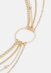 Gold multi-layered necklace featuring various chain styles, including large link, small link, and beaded chains, joined by a circular connector.