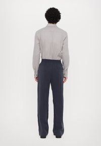 Harmaa pitkähihaisessa paidassa, jossa on napit, yhdistetty tummansinisisiin, rentoihin housuihin, joissa on joustava vyötär�ö, nähtynä takaa.