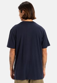 Camiseta de algodón azul marino con un corte relajado, mangas cortas y un sencillo cuello redondo, mostrada desde la parte posterior, con detalles de costura sutiles.