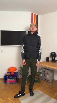 Μαύρο μπουφάν με κουκούλα, με λευκά σχέδια φλόγας στα μανίκια. Συνδυασμένο με πράσινα παντελόνια και μαύρα αθλητικά παπούτσια με λευκές ρίγες.