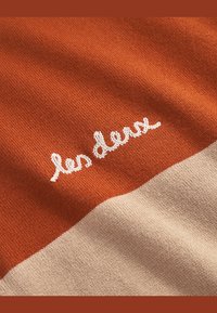 Strikkegenser i oransje og beige striper, med strukturert strikk og brodert logo "les deux" i hvitt.