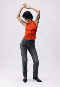 Rdeča rebrasta brezrokavna majica z gumbom spredaj, v paru s sivo visoko pasom hlačami. Model nosi črne škornje z ostro konico.