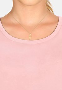 Guldkæde med en fisk-formet vedhæng, båret over en blød pink skjorte. Vedhænget og kæden har en glat overflade og minimalistisk design.