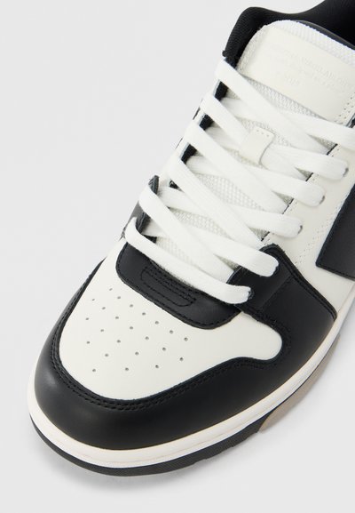 Μαύρο και άσπρο αθλητικό παπούτσι με λείο δερμάτινο πάνω μέρος, διάτρητη μύτη και υφασμένες κορδόνια, με αντιθετικό λαστιχένιο πέλμα.