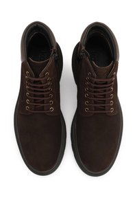 Botas de tobillo de ante marrón con un cuello acolchado, puntera redonda, parte delantera con cordones y ojales en tono dorado. Presenta un zipper lateral y una suela de goma texturizada.