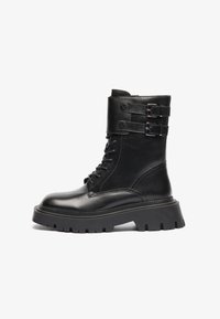Botas de tobillo de cuero negro con punta redondeada, cordones en la parte delantera, bandas de doble hebilla en el puño y una suela gruesa y estampada.