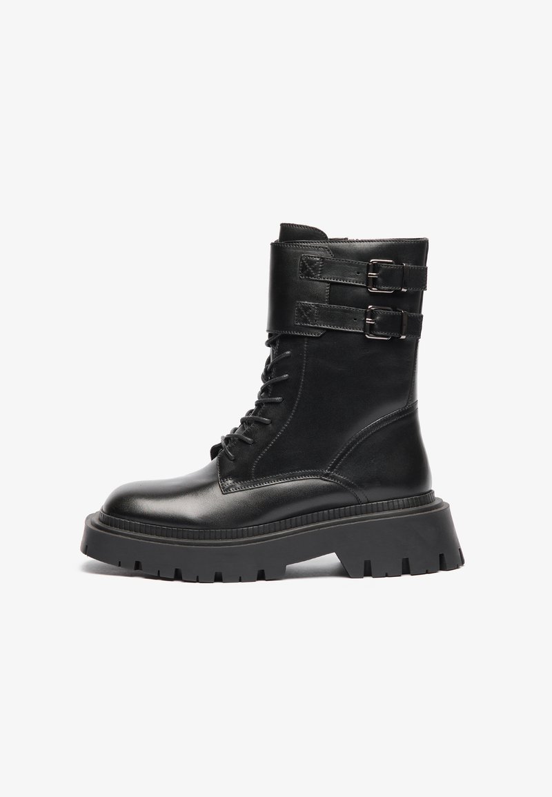 Botas de tobillo de cuero negro con punta redondeada, cordones en la parte delantera, bandas de doble hebilla en el puño y una suela gruesa y estampada.
