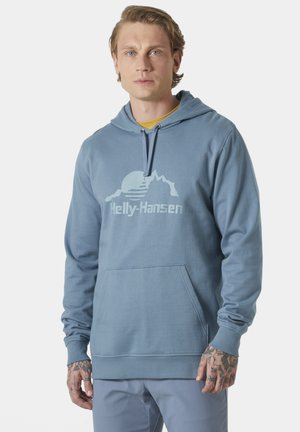 Sudadera azul claro con bolsillo frontal, capucha con cordón y un logotipo gráfico que presenta montañas y un sol en el pecho. Material de mezcla de algodón.