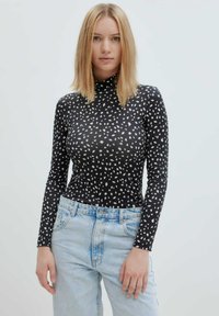 Zwarte lange mouwen coltrui met witte onregelmatige vlekken, gecombineerd met lichtblauwe hoge taille jeans, wat een contrasterende uitstraling creëert.